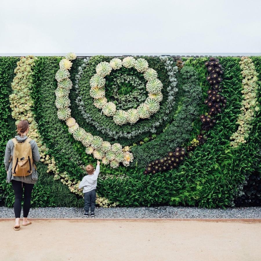 mother and child standing in front of a mural made of plants